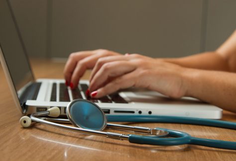 hands on a laptop with a stethoscope next to it