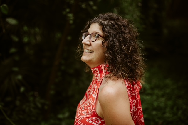 A woman (Karen) with curly hair and glasses smiling in the woods.