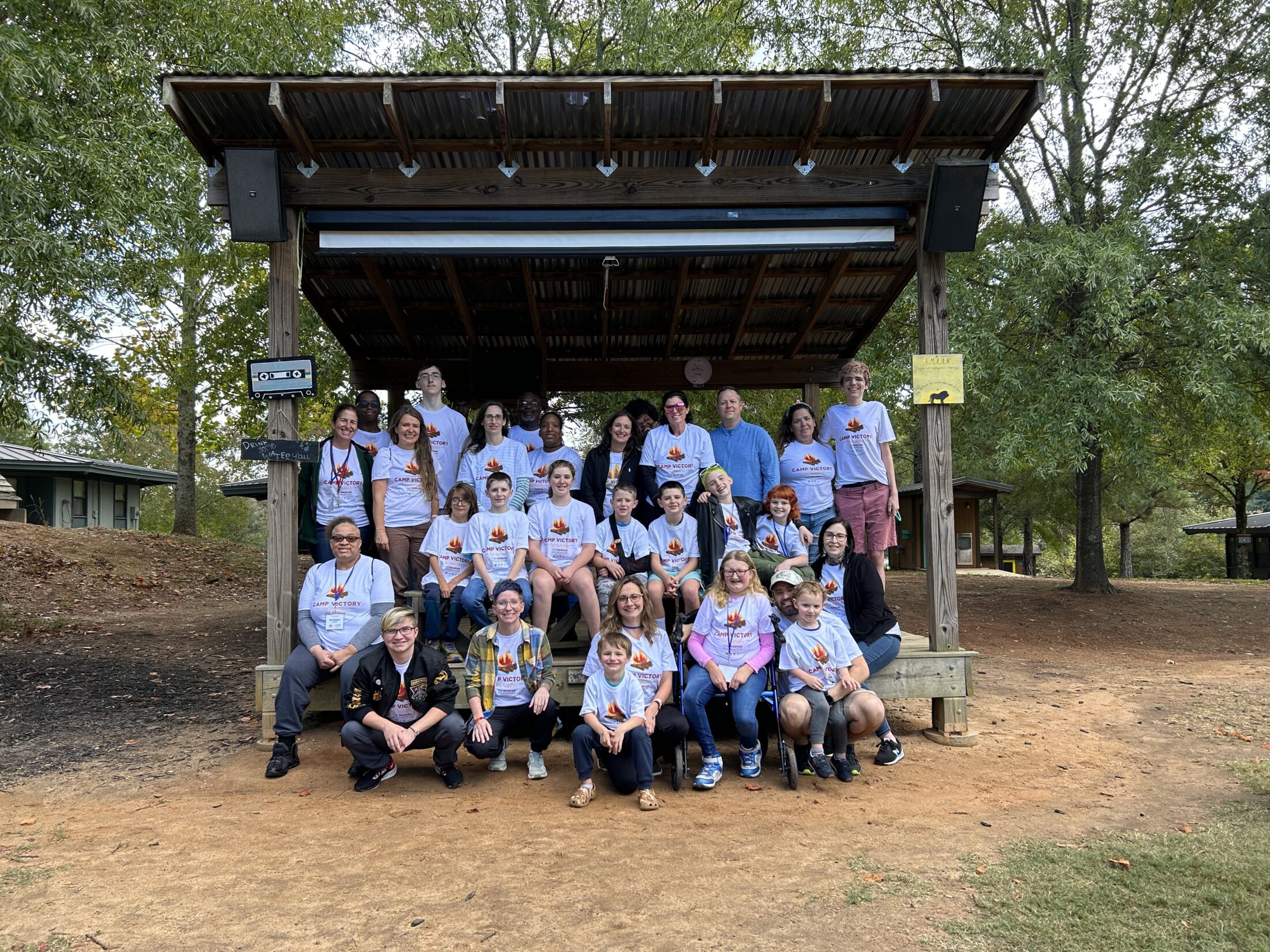 large group photo of camp victory participants in an outdoor shelter structure smiling 