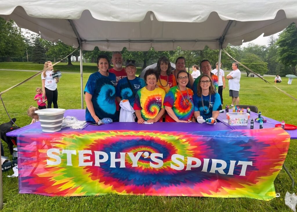 At the 2025 Marfan Foundation New Jersey Walk for Victory, a group is pictured under a tent in tie dye with a banner labeled Stephy's Spirit, honoring the late Stephanie Mahnken.