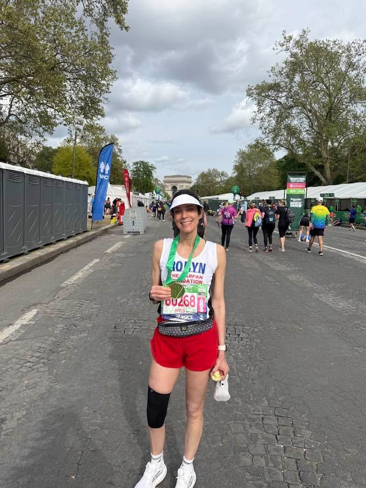 A runner displays her medal after the Paris Marathon and is pictured standing on the concrete. 