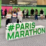 Team Victory runners support the Paris Marathon. A group is pictured with a #ParisMarathon sign in green at the Paris airport.