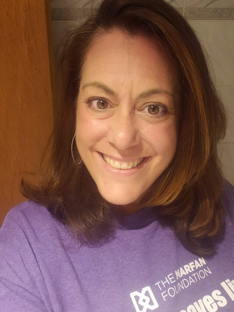Roe Nania is pictured wearing a purple Marfan Foundation tee-shirt and smiling. 