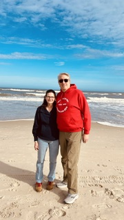 Heidi and Chris Underwood standing side by side on a beach in winter clothes with blue skies behind them