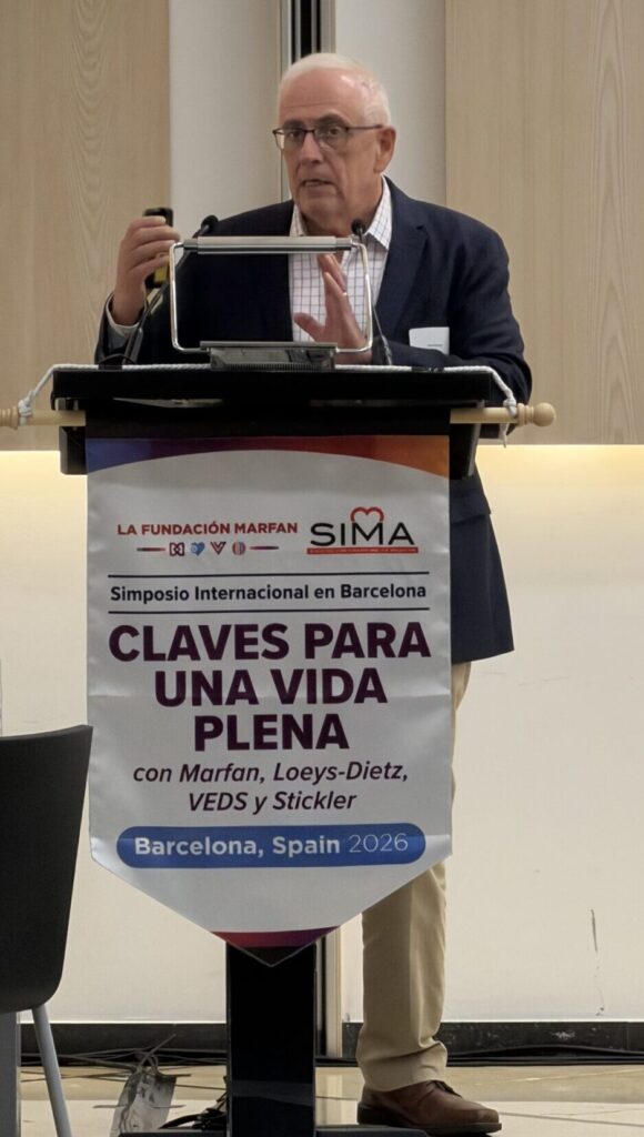 Dr. Juan Bowen of Mayo Clinic speaks at a podium draped with a banner for the symposium "Claves para una vida plena" in Barcelona, Spain, 2026.
